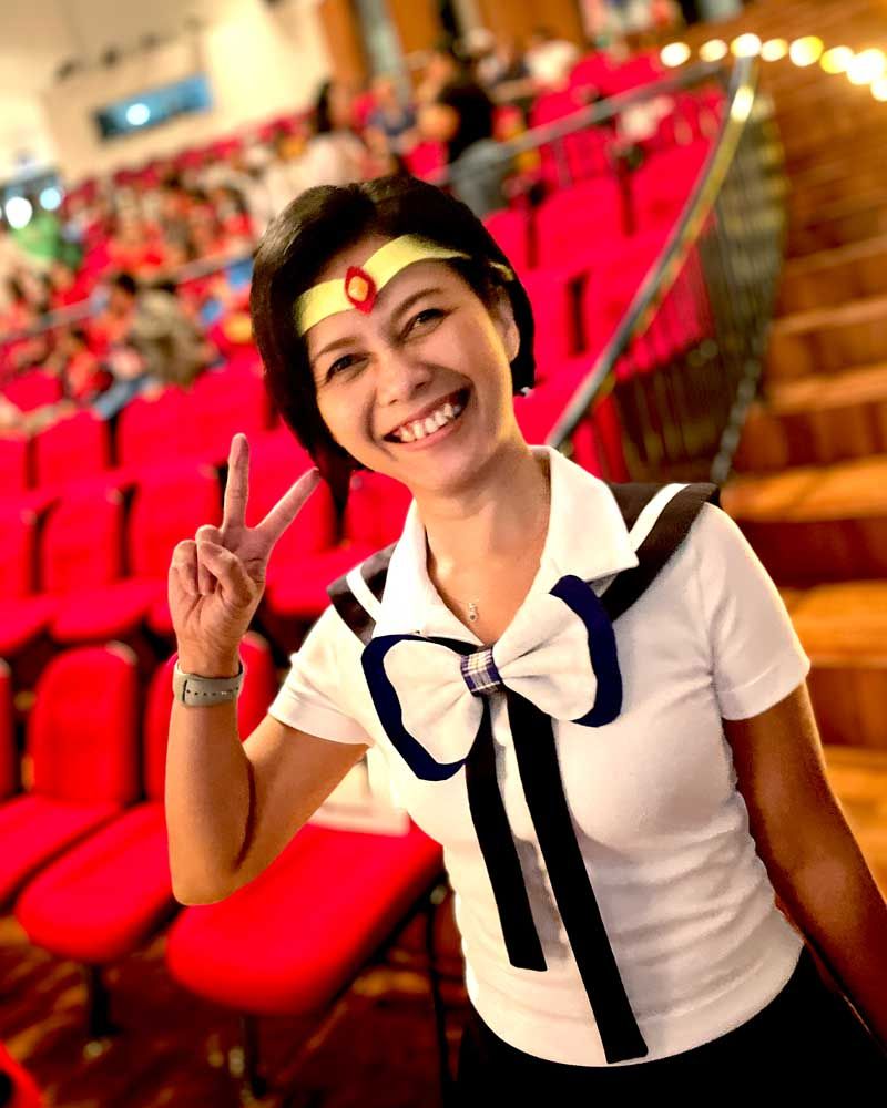 A woman in a white shirt with a bow on it is giving a peace sign
