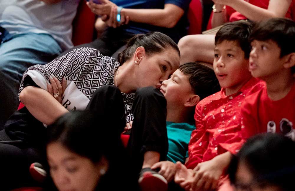 A woman is kissing a child on the cheek while sitting in a crowd of people.