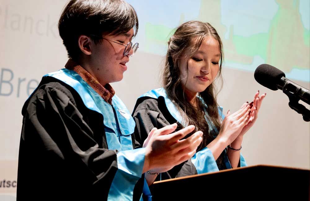 A boy and a girl are standing at a podium clapping their hands.