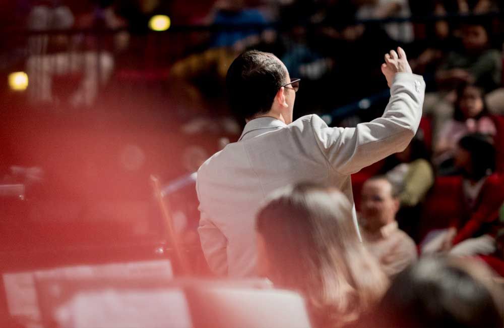 A man in a white jacket is standing in front of a crowd of people.