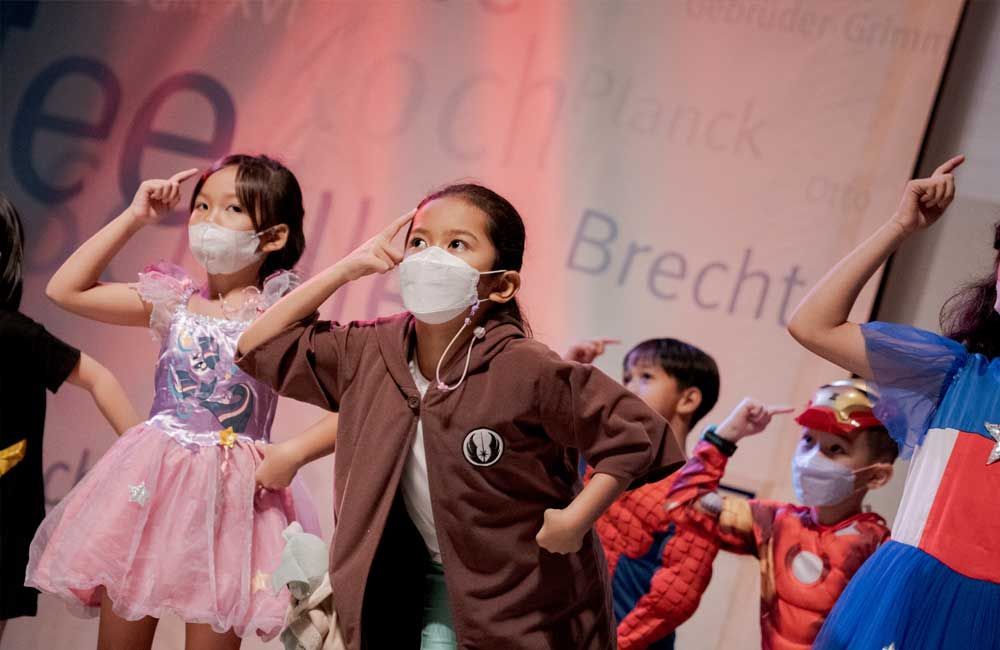 A group of children wearing masks and costumes are dancing on a stage.