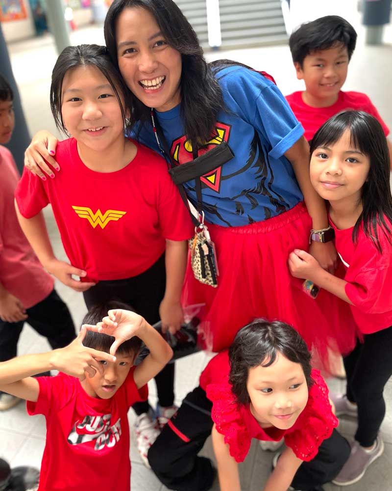 A group of children are posing for a picture with a woman wearing a wonder woman shirt.