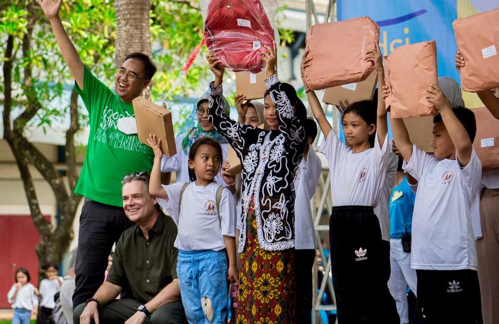 A group of children are standing in front of a man holding a backpack.