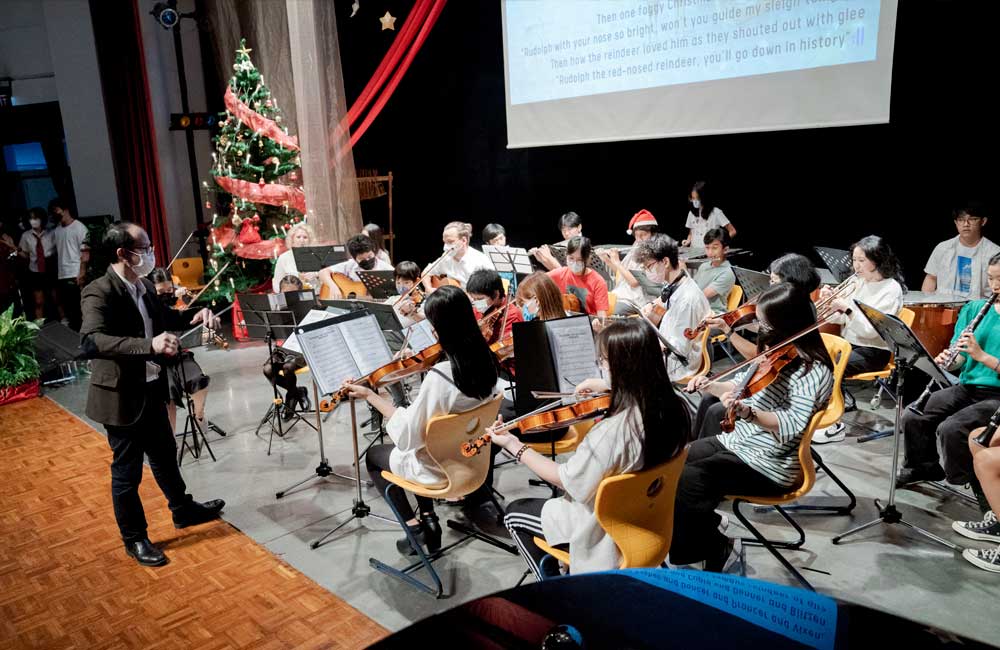 A man is standing in front of an orchestra playing violins and guitars.