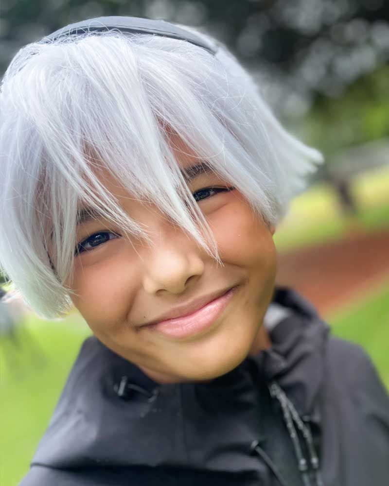 A young boy wearing a white wig and a black jacket is smiling.