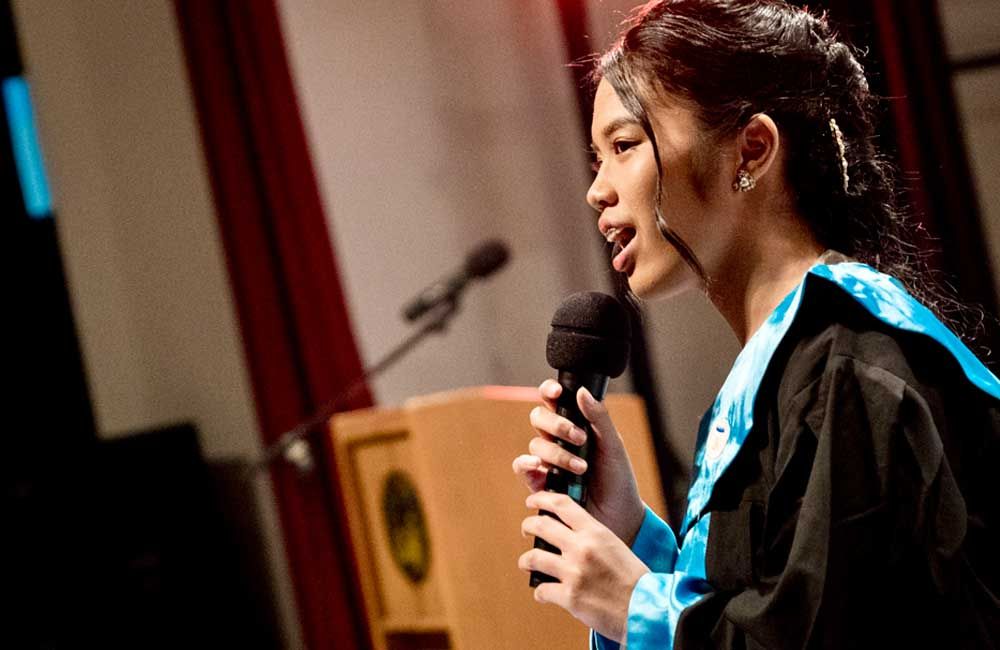 A woman in a graduation gown is singing into a microphone.