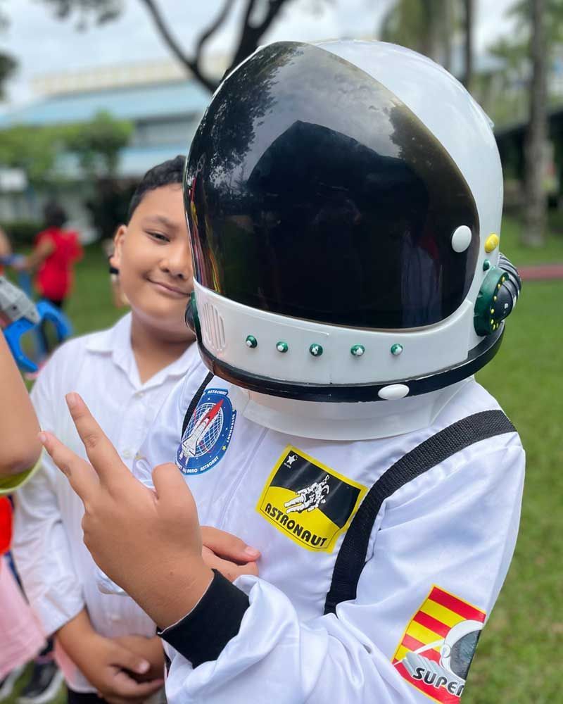 A young boy dressed as an astronaut is giving a peace sign.