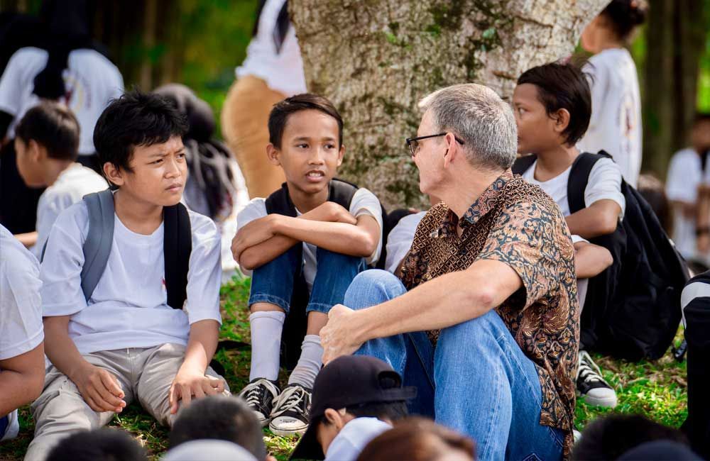 A man is sitting on the grass talking to a group of children.