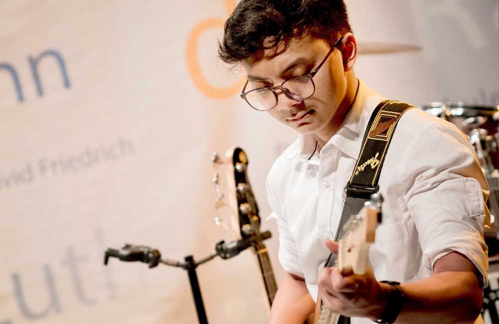 A young man wearing glasses is playing a guitar in front of a microphone.