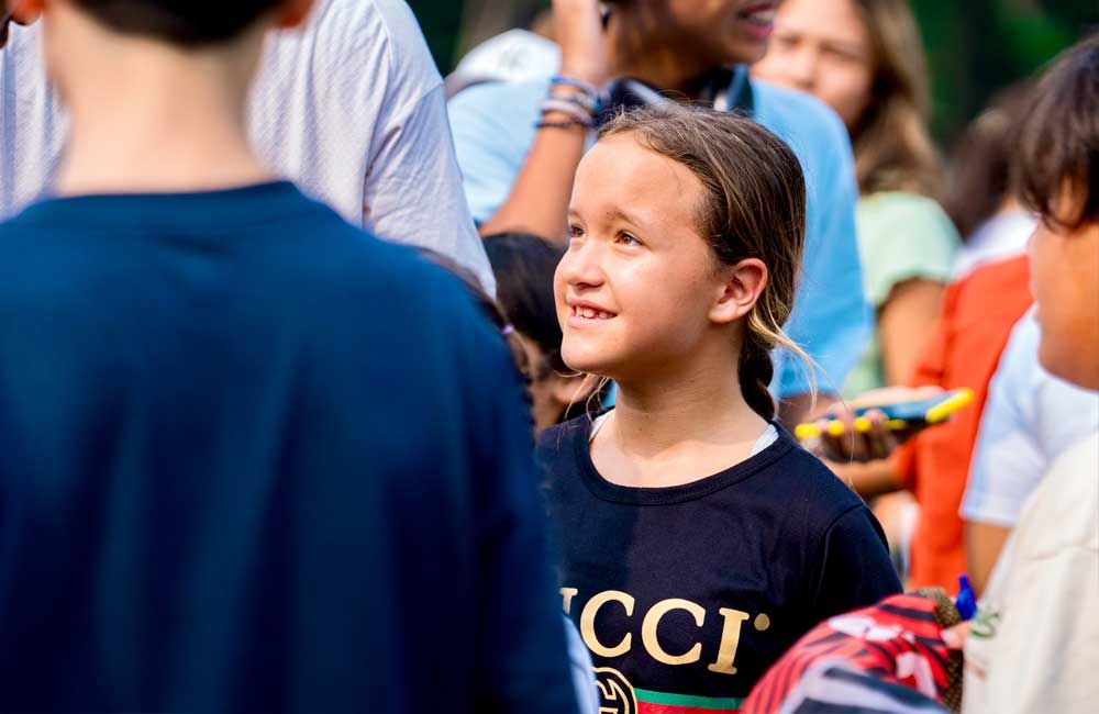 A young girl wearing a gucci shirt is standing in a crowd of people.