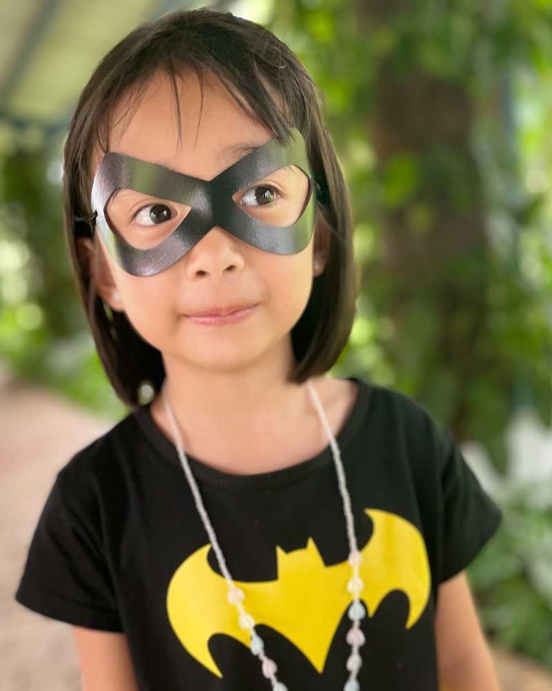 A little girl wearing a mask and a batman shirt