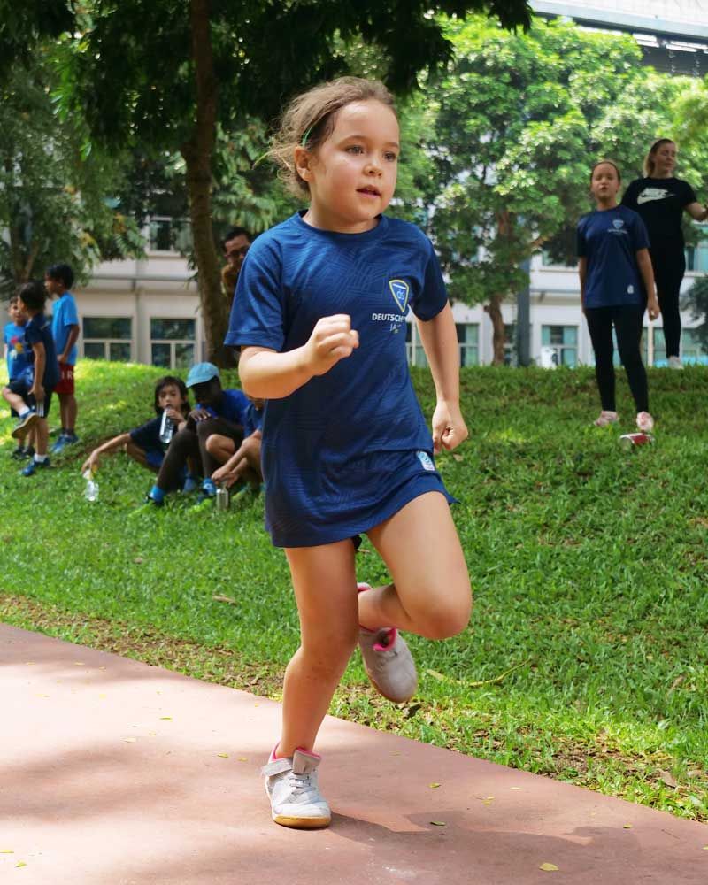 A little girl in a blue shirt is running in a park