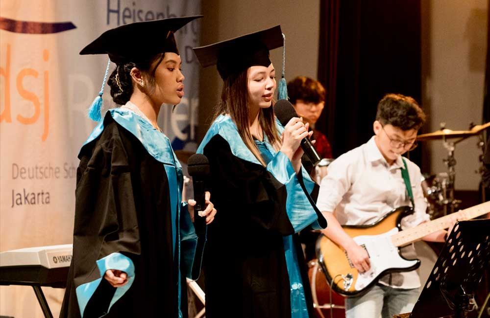A group of graduates are singing and playing instruments on stage.