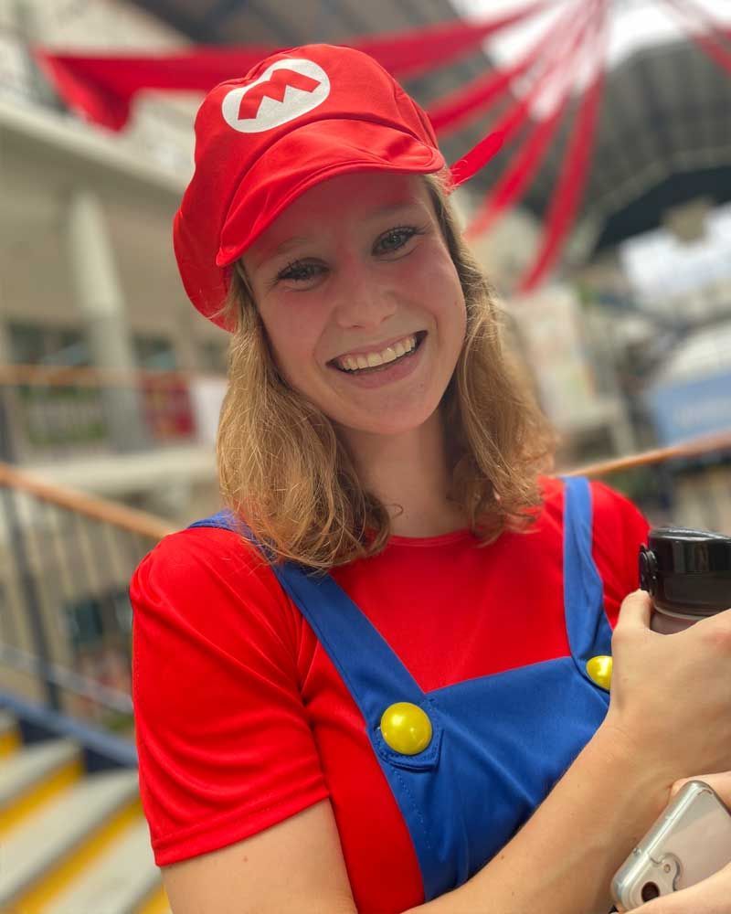 A woman in a mario costume is smiling and holding a cell phone.