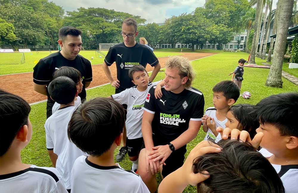A group of young boys are standing around a man on a soccer field.