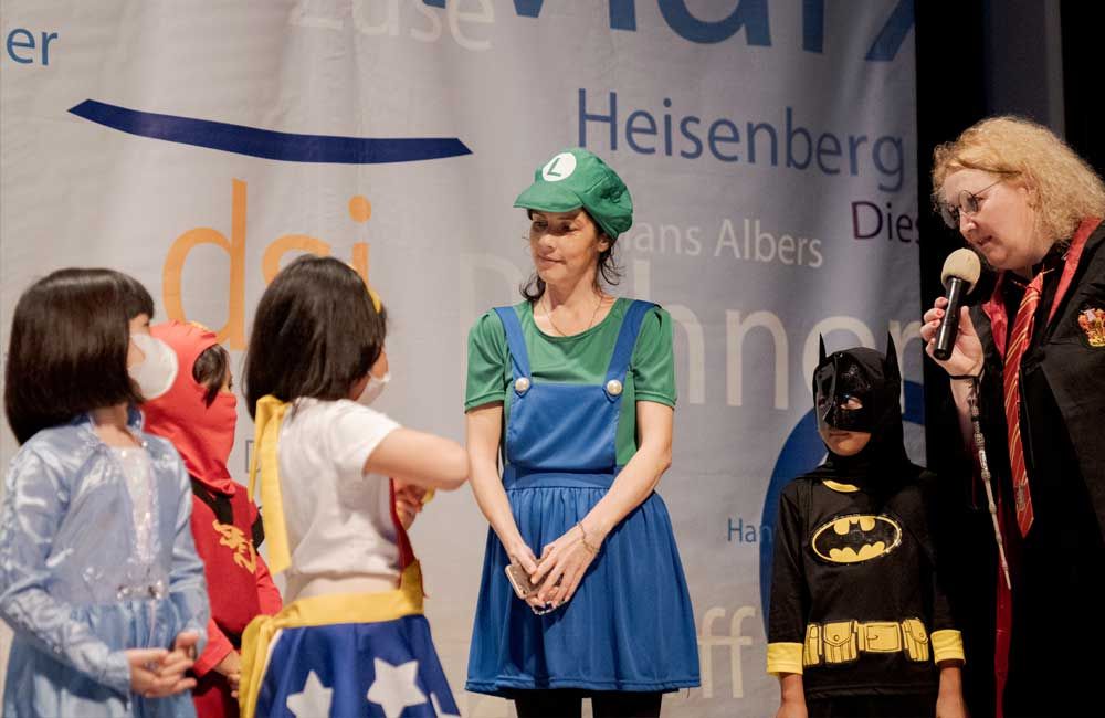 A group of children in costumes are standing in front of a banner that says heisenberg