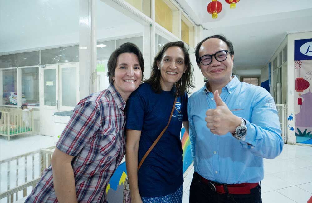 Three people are posing for a picture in a hallway and one of them is giving a thumbs up.