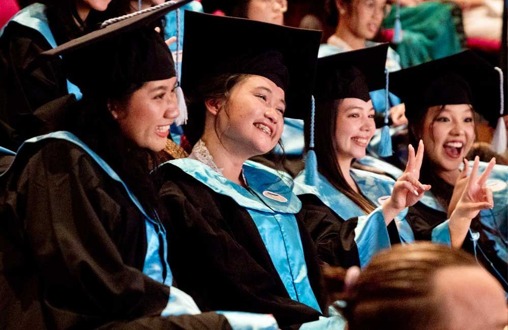 A group of graduates are sitting in a row and smiling.