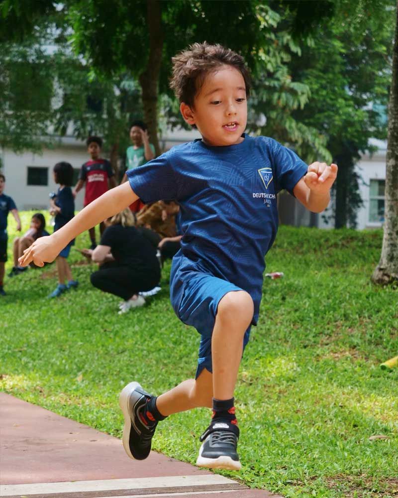 A young boy in a blue shirt is running in a park.
