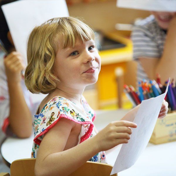 A little girl is sitting at a table holding a piece of paper