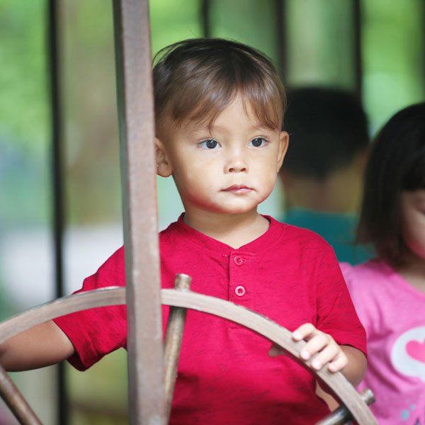 A little boy in a red shirt is holding a wooden steering wheel