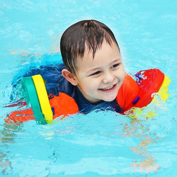 A young boy wearing a life jacket is swimming in a pool.