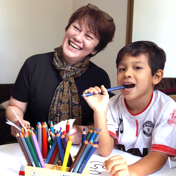 A woman and a boy are sitting at a table with colored pencils