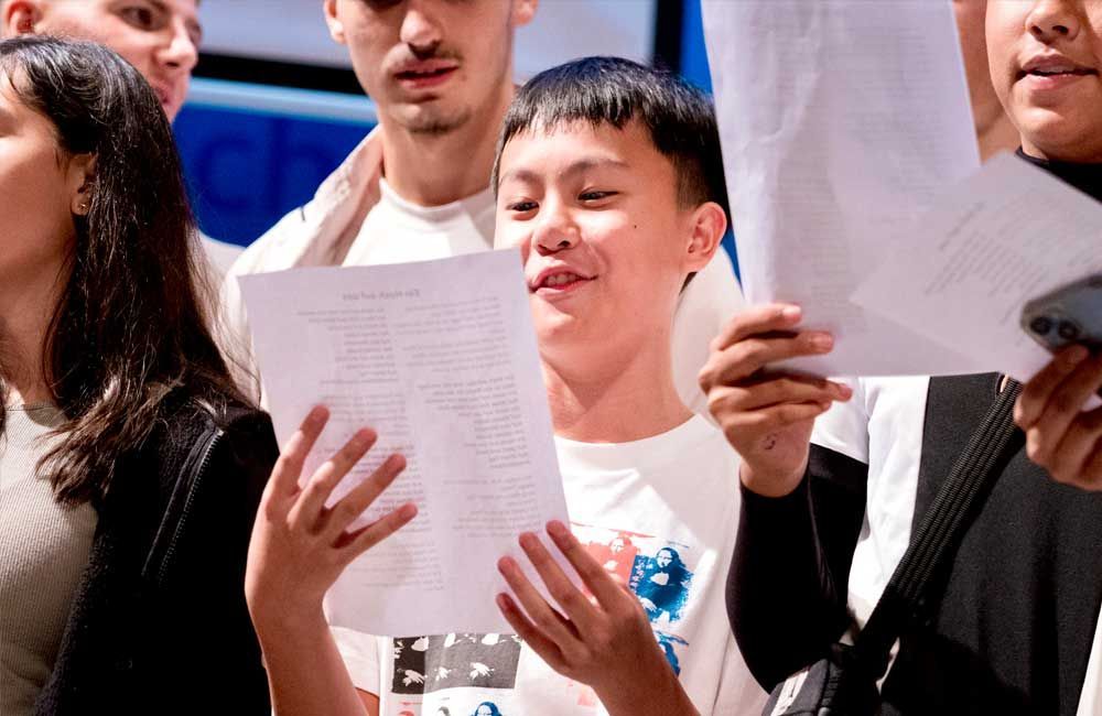 A group of people are singing together while holding papers in their hands.