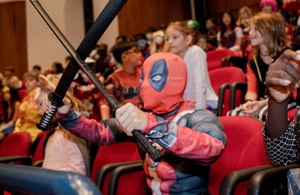 A child dressed in a Deadpool costume holding two swords.