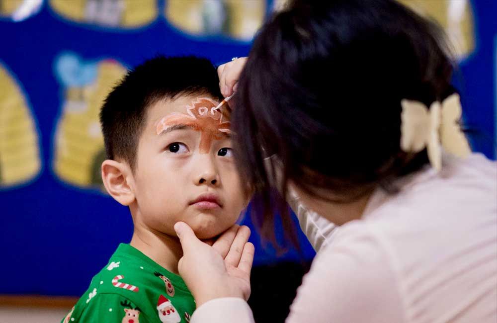 A little boy is getting his face painted by a woman.