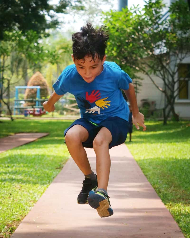 A young boy in a blue shirt is jumping in the air