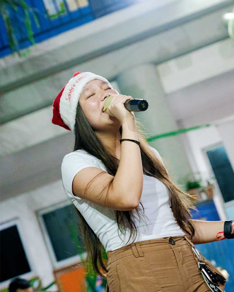 A woman wearing a santa hat is singing into a microphone.