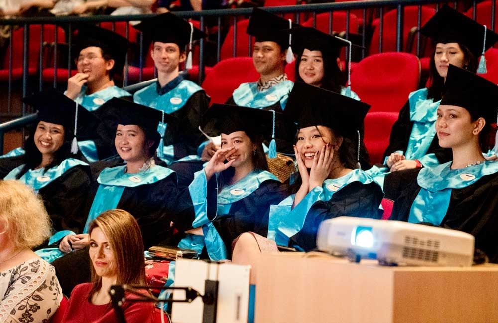 A group of graduates are sitting in a auditorium in front of a projector.