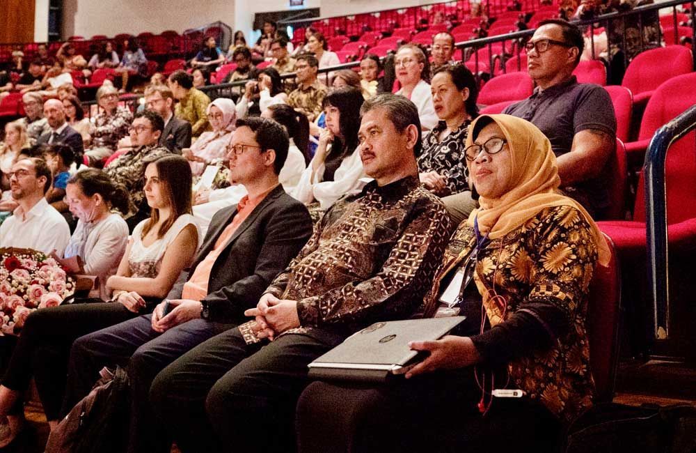 A group of people are sitting in red seats in an auditorium.