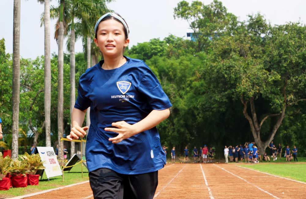 A young girl in a blue shirt is running on a track.