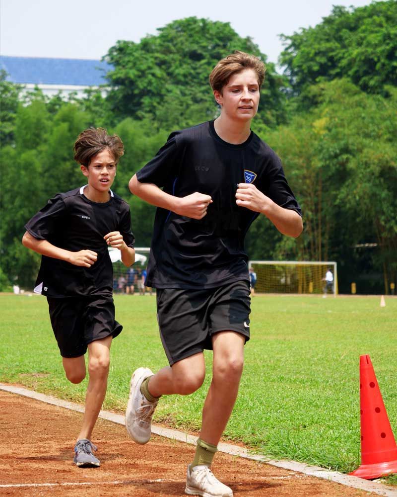 Two young boys are running on a track in a field