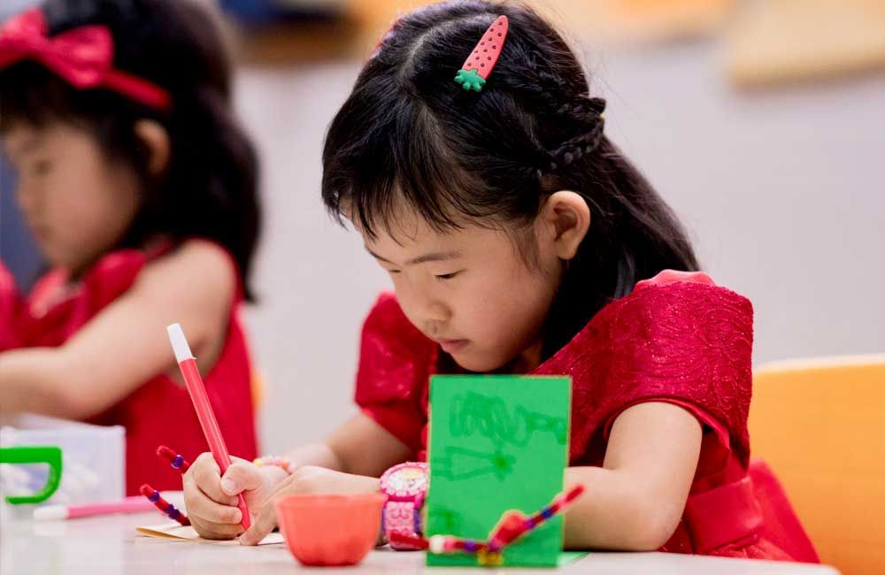 Two little girls are sitting at a table drawing with pencils.