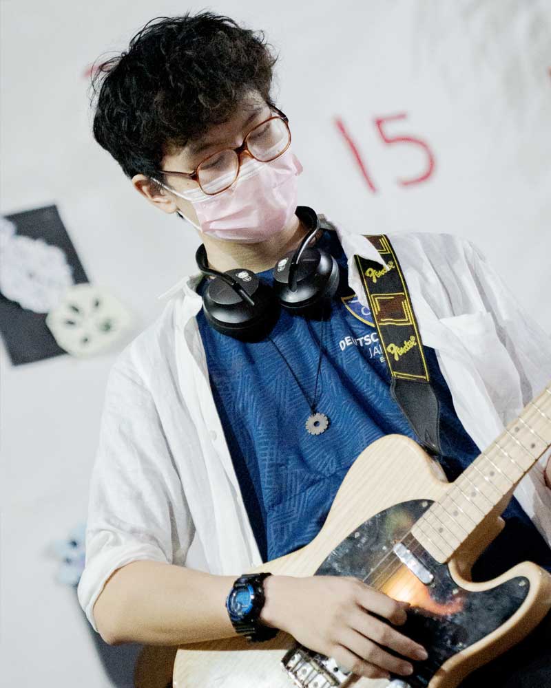 A young man wearing a mask and headphones is playing a guitar.