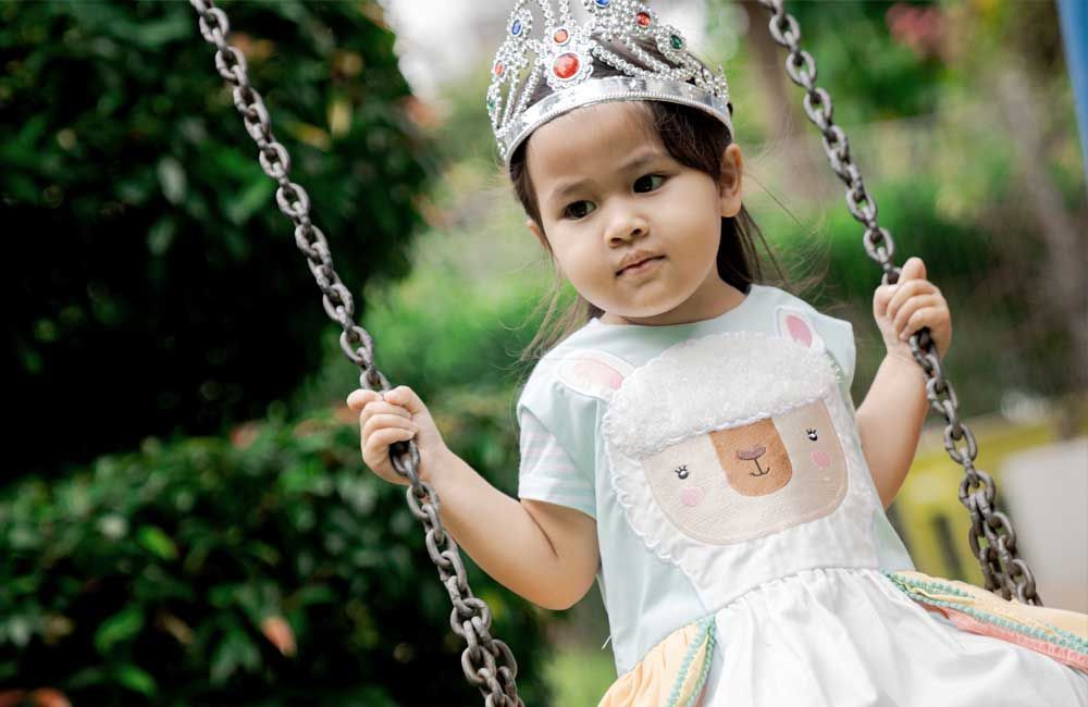 A little girl wearing a crown is sitting on a swing.
