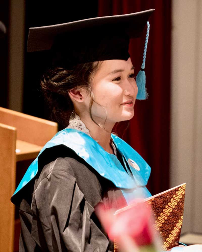 A woman in a graduation cap and gown is smiling