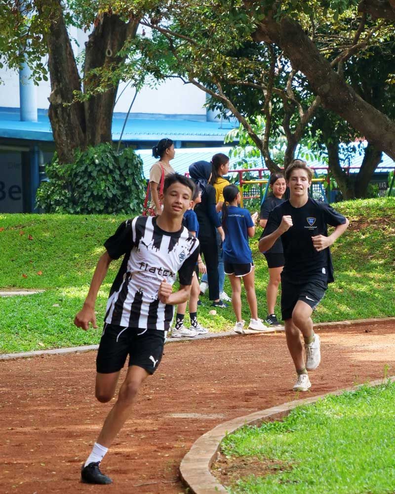 A boy in a black and white striped shirt is running on a track