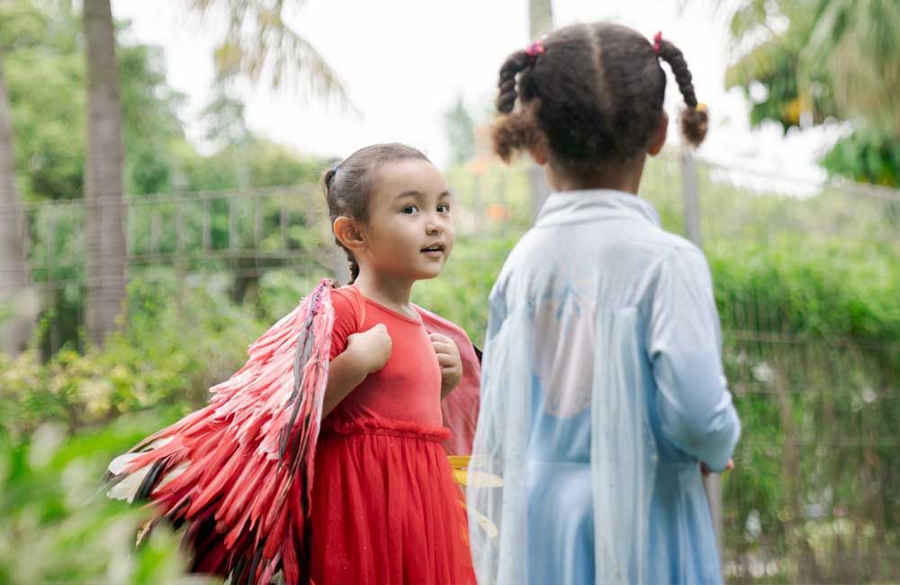 Two little girls are standing next to each other in a park.