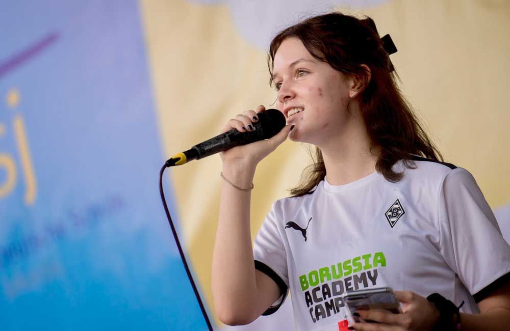 A woman in a borussia academy shirt is singing into a microphone.