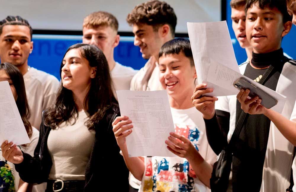 A group of young people are singing and holding papers in their hands.