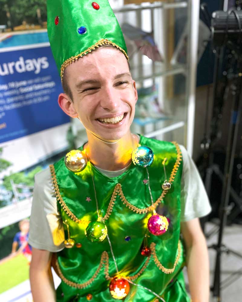 A man is wearing a green christmas tree costume and smiling.