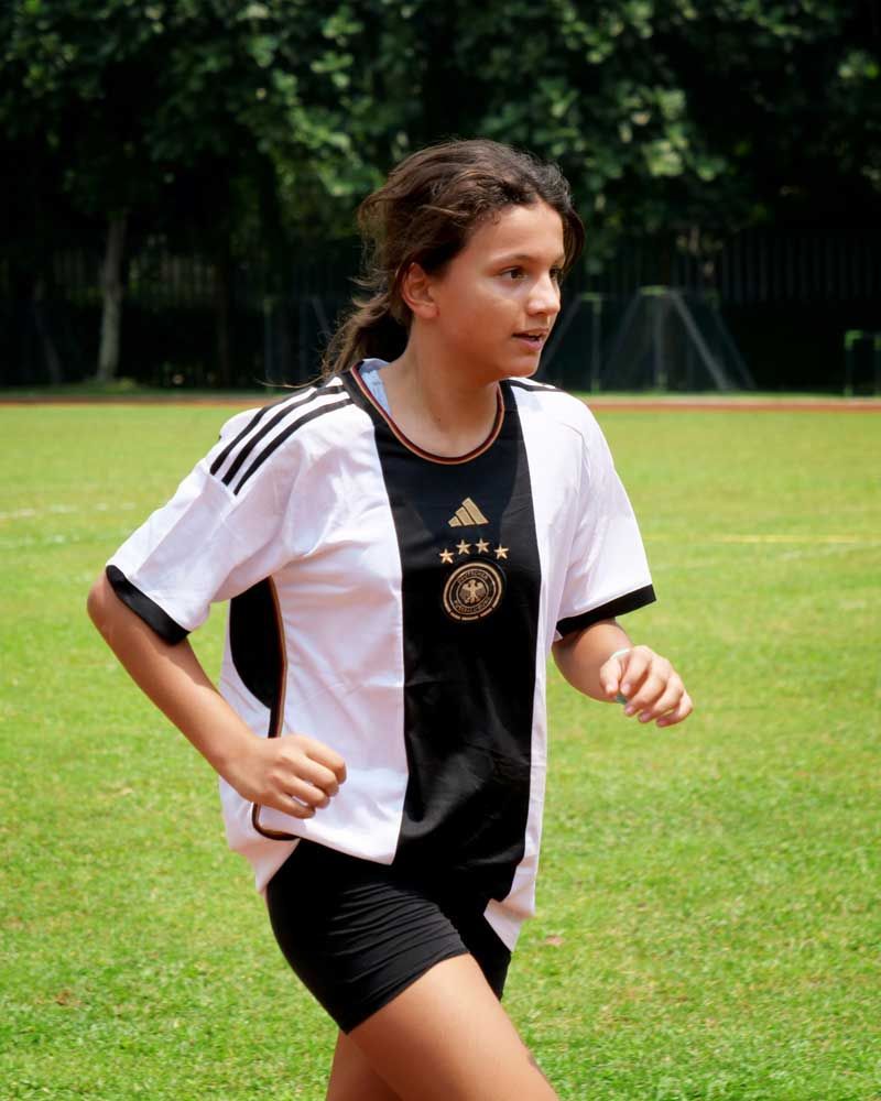 A girl in a black and white adidas shirt is running on a field