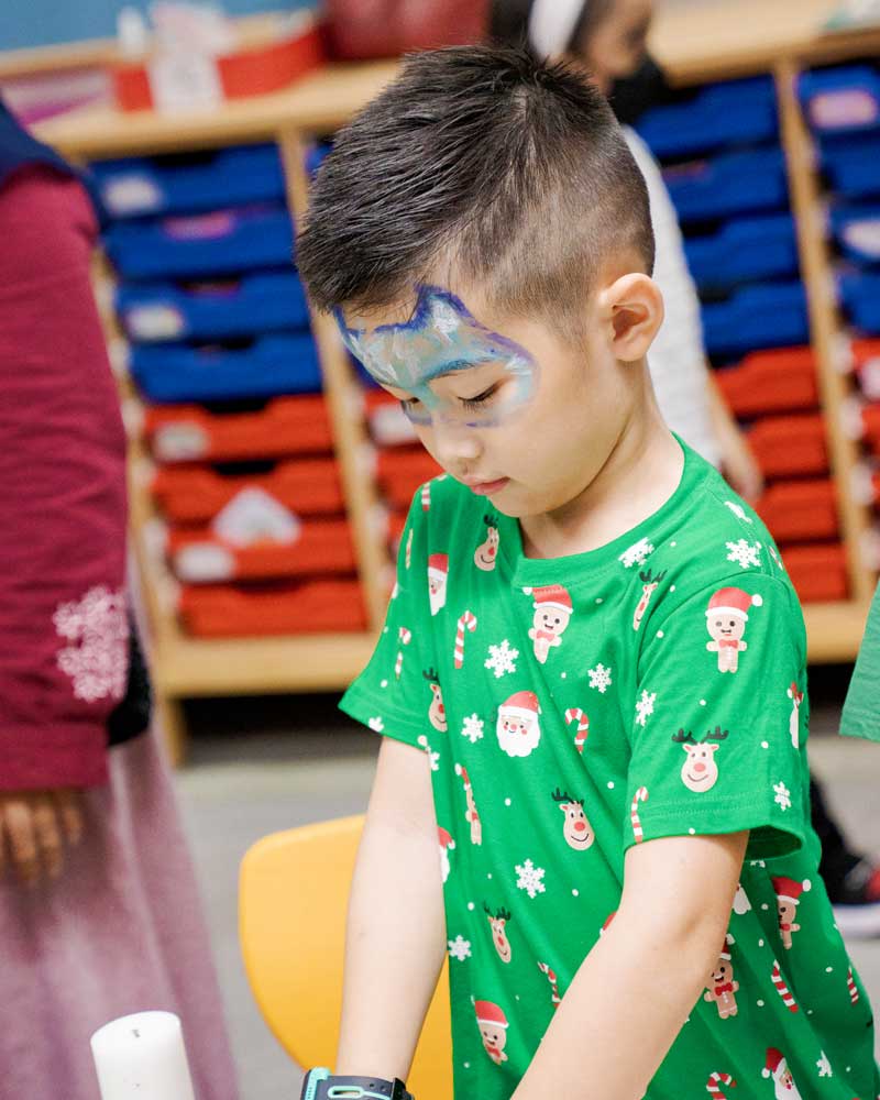 A young boy with a cat painted on his face is wearing a green shirt.