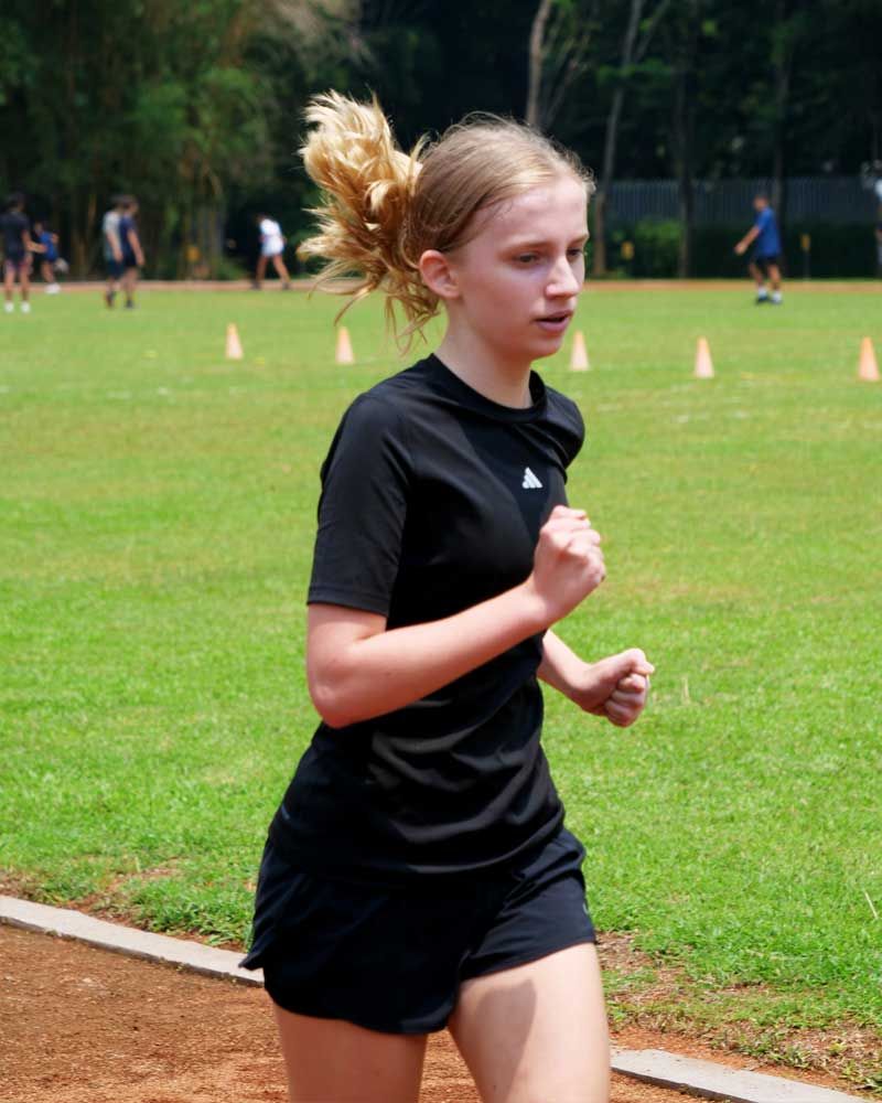 A young girl in a black adidas shirt is running on a track