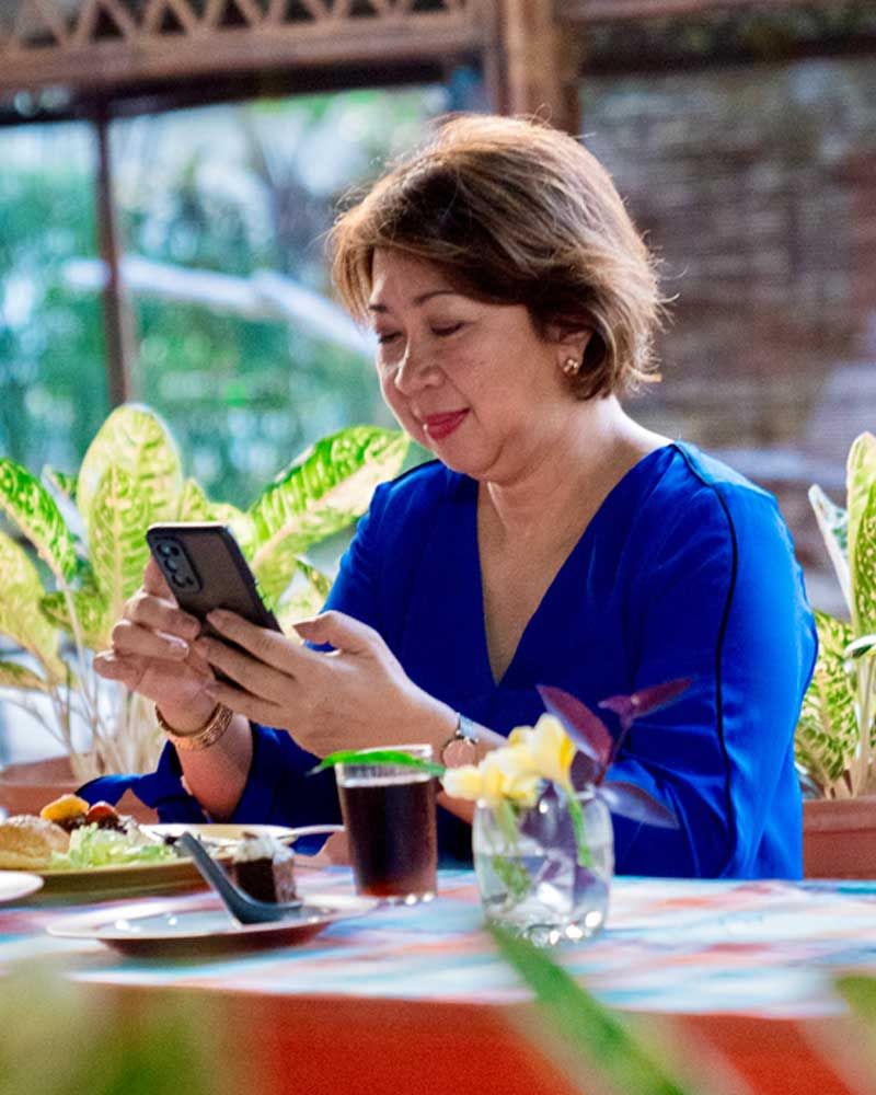 A woman in a blue shirt is sitting at a table looking at her phone.