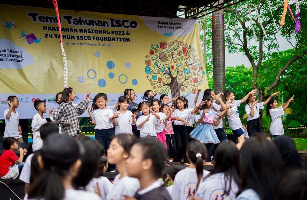 A group of children are dancing in front of a large yellow banner.